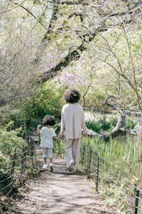 A serene moment of a mother and child walking on a spring forest path, surrounded by lush greenery.