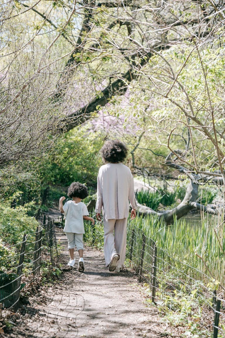 A serene moment of a mother and child walking on a spring forest path, surrounded by lush greenery.
