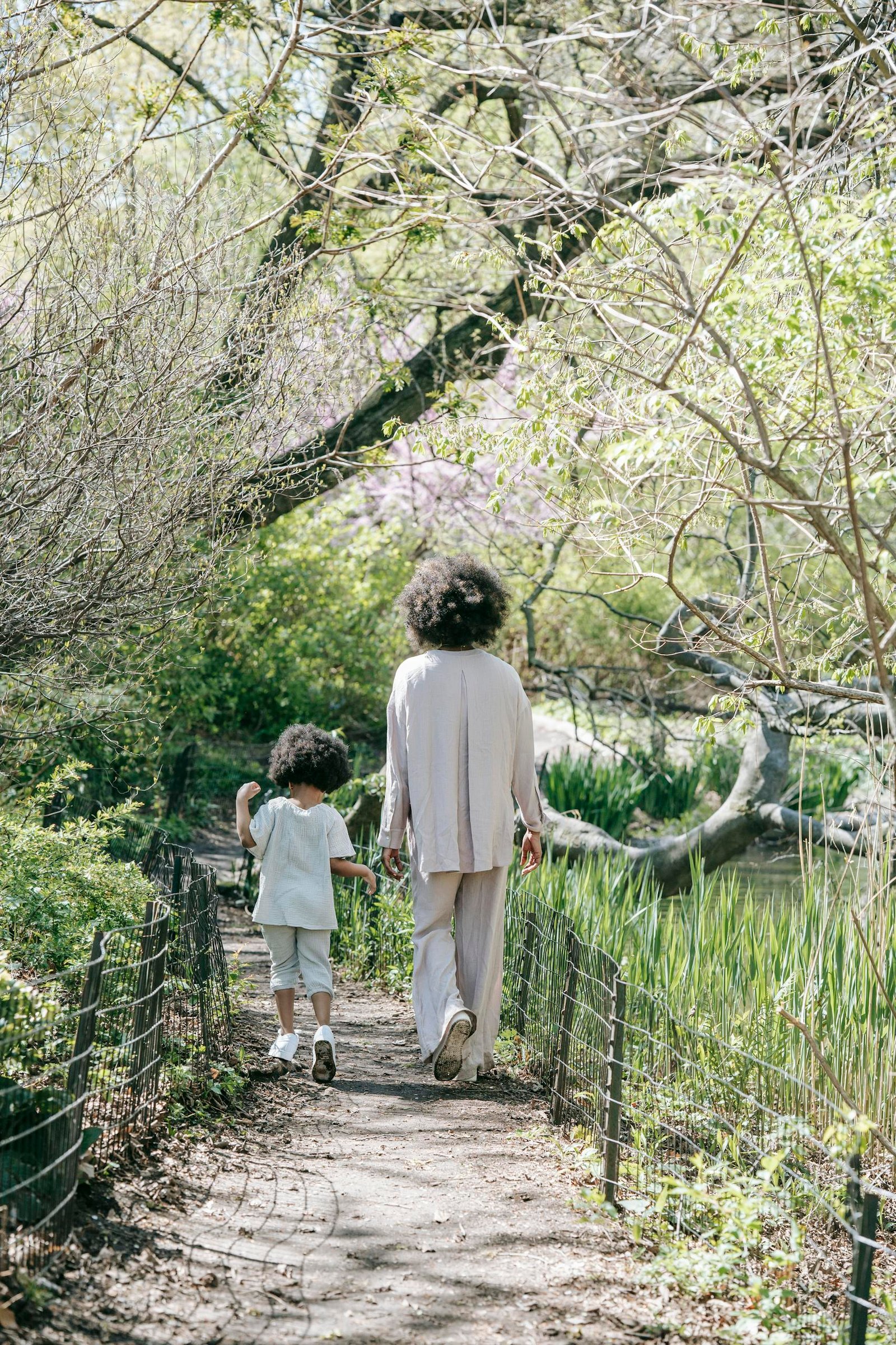 A serene moment of a mother and child walking on a spring forest path, surrounded by lush greenery.